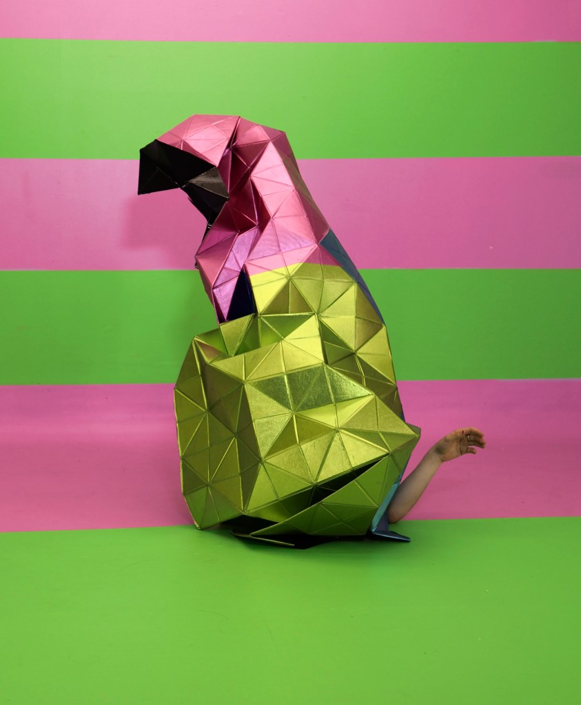 pink and green metallic sculpture folded like a creature with arm at the base like a tail, on pink and green background