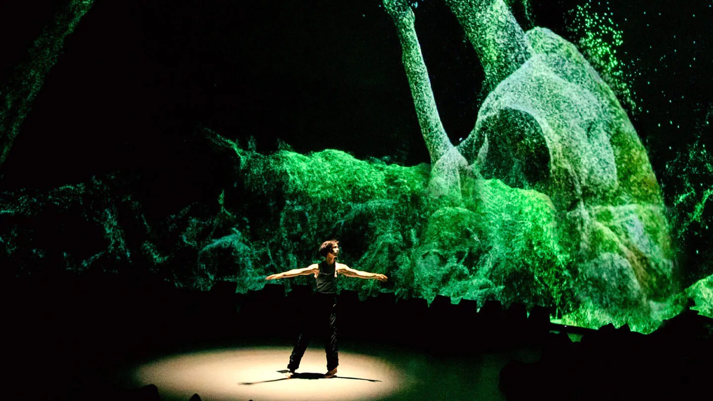 Dancer, Lucy Fandel standing arms out like T, against a digital landscape of green particles.