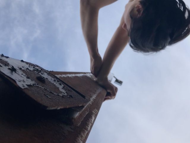 Against a blue-white sky, Lucy's pressing her hands agains a rusty telephone pole